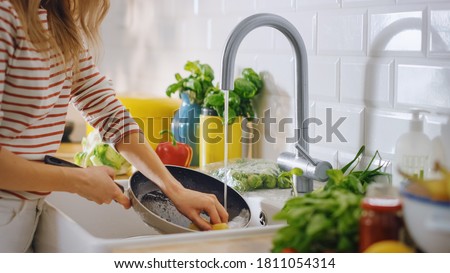 Close Up Shot of a Woman Washing a Frying Pan with a Cleaning Liquid Under Tap Water. Using Dishwasher in a Modern Kitchen. Natural Clean Diet and Healthy Way of Life Concept. Royalty-Free Stock Photo #1811054314