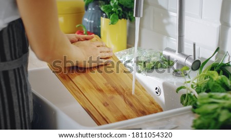 Close Up Shot of a Person Washing a Chopping Board with a Cleaning Liquid Under Tap Water. Using Dishwasher in a Modern Kitchen. Natural Clean Home and Healthy Way of Life Concept. Royalty-Free Stock Photo #1811054320