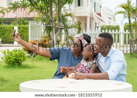 African American family spending time together in the garden. They have a bright and happiness. is taking pictures of the family with a smartphone.