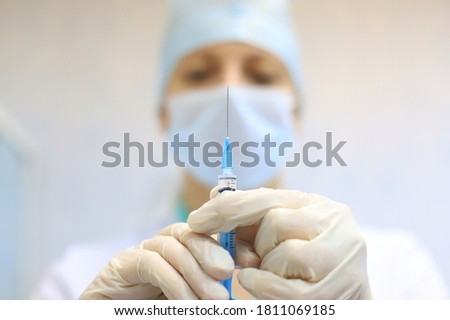 A nurse (face blurred) holds a syringe filled with medication before the injection (close-up)