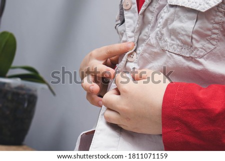 Childhood independence concept ,little boy buttoning on shirt, fastening his buttons , on white gray background. The child puts on his own clothes