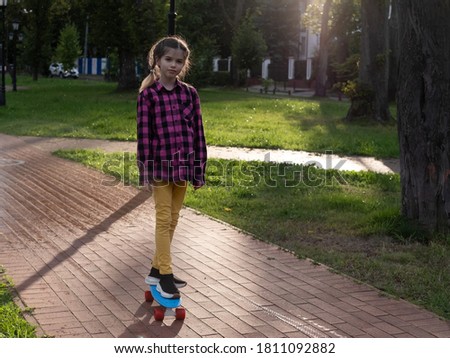little / young girl rides a skateboard in the park on a summer evening at sunset in the sun