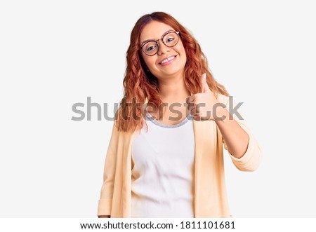 Young latin woman wearing business clothes doing happy thumbs up gesture with hand. approving expression looking at the camera showing success. 