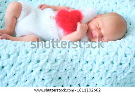 A sleeping newborn boy or girl lies on blue wool. Heart shape red fluffy soft pillow or cushion for Valentine's day love