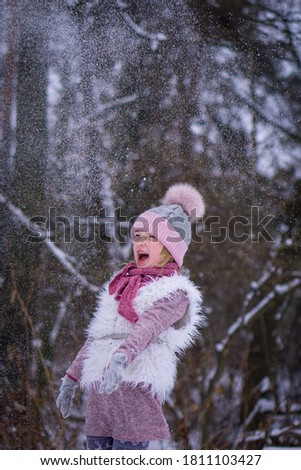 girl child in a pink hat and vest rejoices in the snow