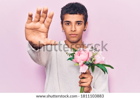 Young african amercian man holding flowers with open hand doing stop sign with serious and confident expression, defense gesture 