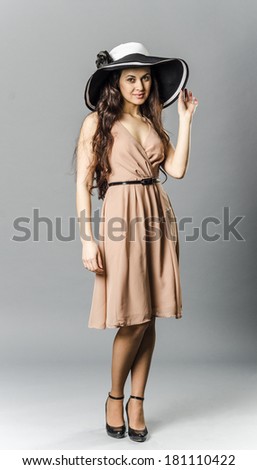 beautiful slender brunette actress in the summer beige dress and hat standing relaxed coquettishly
