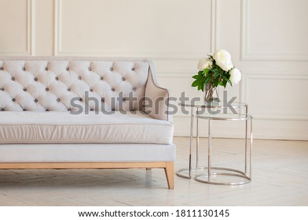 Modern Spacious minimalistic living room interior with a gray sofa and a coffee table with a vase with a bouquet of peonies flowers against a white wall. Scandinavian  interior home. Cozy room decor.
