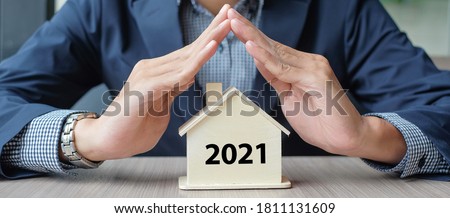 Businessman hands over wooden House model with 2021 New Year text. Property insurance and real estate concepts Royalty-Free Stock Photo #1811131609