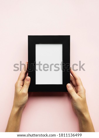 female hands holding black photo frame with blank space on pink background