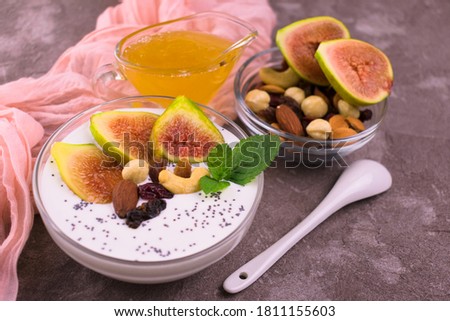 
Greek yogurt with figs, nuts and honey in a bowl on a gray background.
Healthy breakfast concept.
