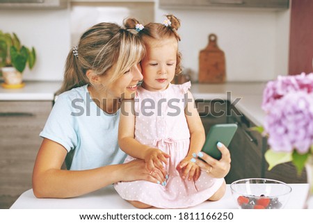 Portrait of a young girl and her little daughter watching a video on their phone while squatting on the floor Royalty-Free Stock Photo #1811166250