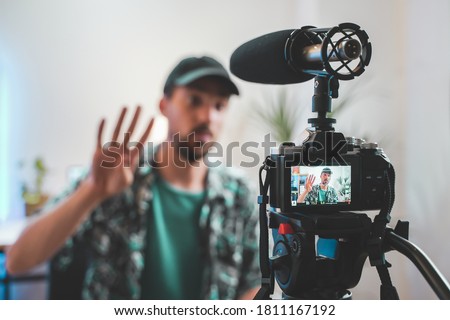 Behind the scene shot of a young man influencer making a video. Very handsome man with beard shooting a video for social media talking directly to the camera. Influencer's amazing work space. Royalty-Free Stock Photo #1811167192