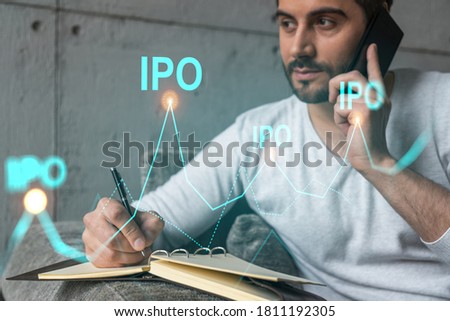Handsome analyst in casual long sleeve talking phone, taking notes at office workplace try to analyze IPO project. Double exposure. Initial public offering hologram. Royalty-Free Stock Photo #1811192305