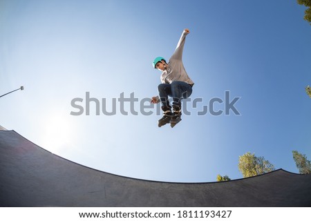 young male inline skater in skate park, in the air doing a jump trick. with protective helmet. rollerblade