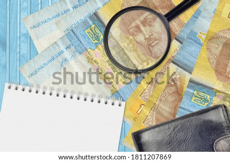 1 Ukrainian hryvnia bills and magnifying glass with black purse and notepad. Concept of counterfeit money. Search for differences in details on money bills to detect fake
