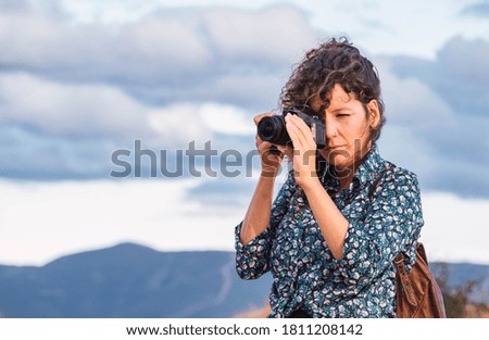 Curly haired woman with a photo camera and backpack traveling in nature. Digital nomad, blogger	