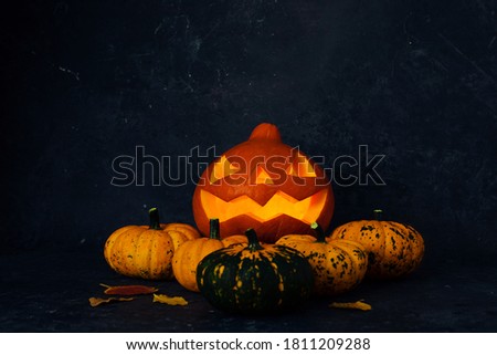 Creative autumn composition. Jack-o ' - lantern with burning candles and colored pumpkins on a dark background, with space to copy 