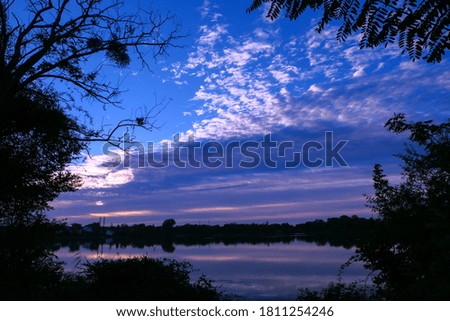 Symmetry of the sky in a lake at sunrise. Clouds reflecting on the water. Holiday landscape by the sea. Quiet relaxing scene. Silhouette of vegetations in foreground. 