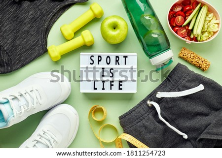 Creative flat lay of sport and fitness equipments and Lightbox with sports slogan. Women's white sneakers, water bottle, sportswear, dumbbells and lunchbox with healthy vegetable salad.