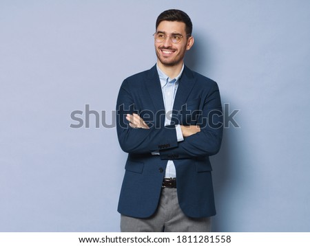 Modern business man standing in smart casual suit, holding crossed arms, smiling and looking aside, isolated on blue background, copy space on left Royalty-Free Stock Photo #1811281558