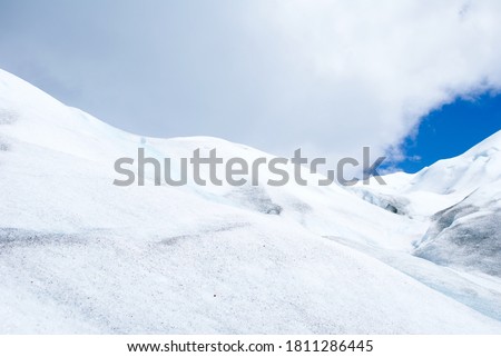 Nieve y hielo acumulado en el glacial, nubes en el cielo con leve zona despejada de cielo azul