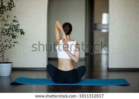 A girl on sport mat performs an exercise of hand to lock behind her back. View from the back. Royalty-Free Stock Photo #1811312017