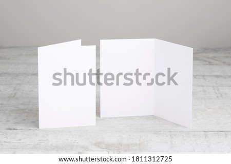 Two white greeting cards mockup, standing upright on a white wooden desk. Blank, open and closed cards template.  Royalty-Free Stock Photo #1811312725