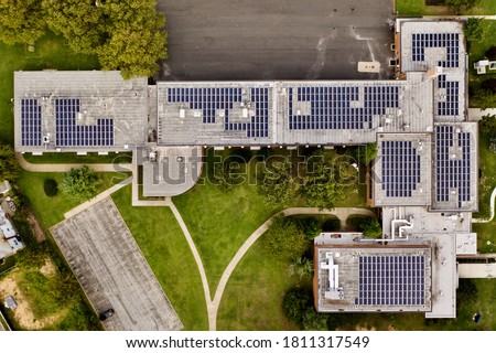 A top down shot directly above a school building during the day. It has many solar panels on the roof. The surrounding grass is green, clean and they are obviously environmentally friendly.