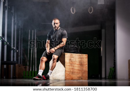 Muscular athlete with weightlifting equipment. Trainer in a fitness studio. Smoke background.