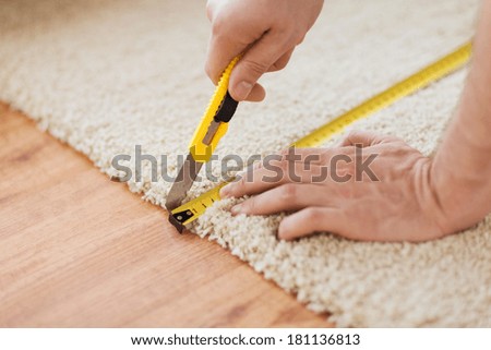 repair, building and home concept - close up of male hands cutting carpet with blade Royalty-Free Stock Photo #181136813
