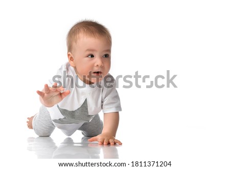 Handsome barefoot baby boy in casual jumpsuit crawling fast on all fours. Cute toddler child creeping on floor looking forward. Confident concentrated kid studio portrait with free text copy space