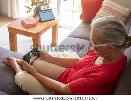 Defocused senior woman red dressed using smart phone to video call with her husband absent due to coronavirus - on the screen smiling lbearded man doing heart shape with hand