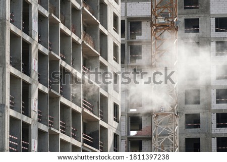 View of the facade of a multi-storey concrete monolithic building under construction. Fences and metal structures on the floors. Cement dust is flying in the air. High quality photo
