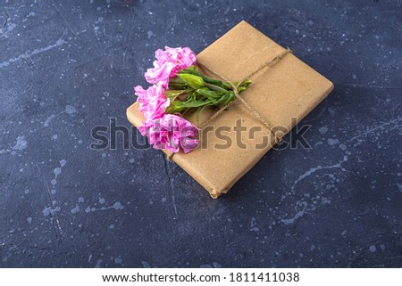 Romantic vintage still life with pretty gift box wrapped with craft paper and decorated with pink flower on dark background. Holiday gift concept. Copy space for text