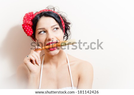 closeup portrait of beautiful charming young brunette woman pin-up girl bites paint brush & looking up on white background