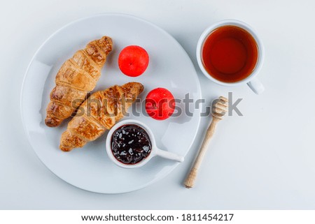 Croissant with jam, plums, dipper, tea in a plate on white background, flat lay. 
