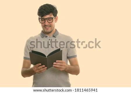 Studio shot of young happy Persian man smiling while reading book