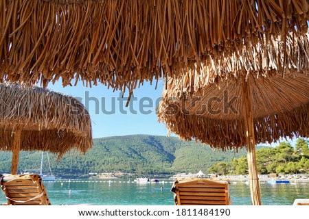 Bamboo umbrellas on a white beach with emerald water, yachts and green hills in the background. Luxury Tourism conception
