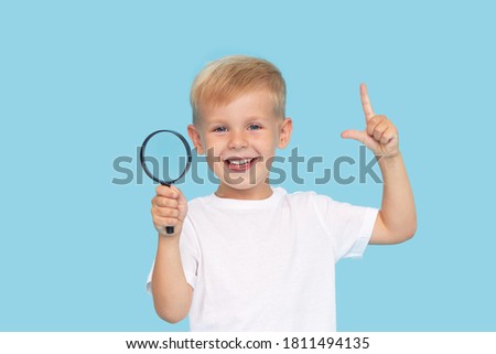 Cute child boy with magnifying glass on blue background. Investigation and discovery concept. 