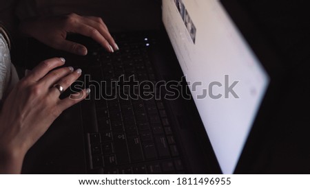 Girl looking for articles and photos on the Internet, in the dark under the blue light of the moon. Fingers working on the keyboard. Freelance work. Computer. Night. Writing an article, a letter