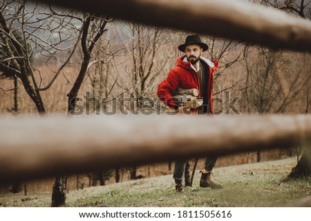 Hipster with beard,  Man in hat and warm jacket chopping and preparing firewood for picnic Royalty-Free Stock Photo #1811505616