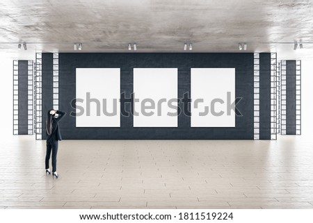 Businesswoman standing in modern gallery interior with three empty billboards on wall. Art and design concept. Mock up,