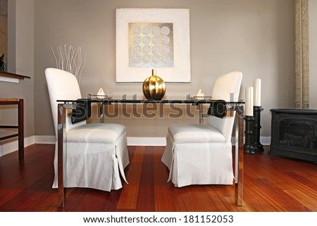 Elegant glass table with white luxury chairs in modern reconstructed living room. Decorated with vase and plates