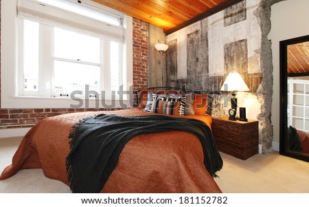 Modern bedroom with brick trim, concrete broken wall and wood plank paneled ceilling. Furnished with iron bed and nightstand.