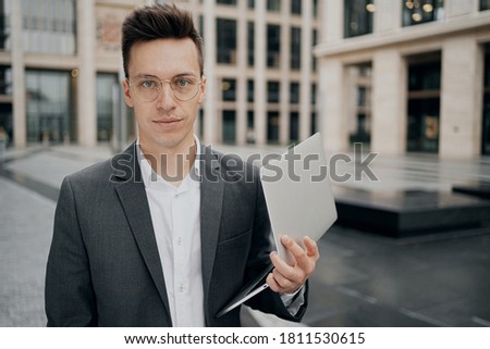 portrait of Caucasian appearance, holding a laptop. gray business suit, standing near the business center. smile on your face