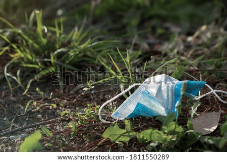 Dirty used medical face mask on the ground among grass as result of covid-19 epidemic time. Environmental pollution. Ecology concept Royalty-Free Stock Photo #1811550289