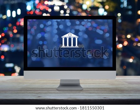 Bank flat icon on desktop modern computer monitor screen on wooden table over blur colorful night light traffic jam road in city, Business banking online concept
