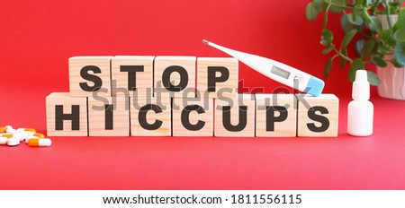The words STOP HICCUPS is made of wooden cubes on a red background with medical drugs. Medical concept.