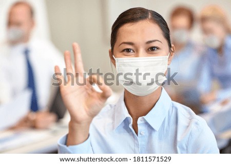 business, people and pandemic concept - businesswoman wearing face protective medical mask for protection from virus disease showing ok sign at office